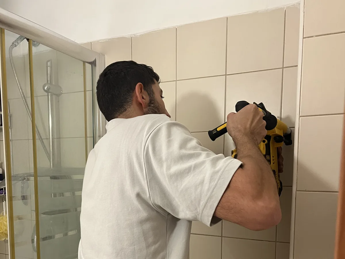 רועי בראון קודח לקיר קרמיקה באמבטיה בתל אביב עם מקדחה נטענת