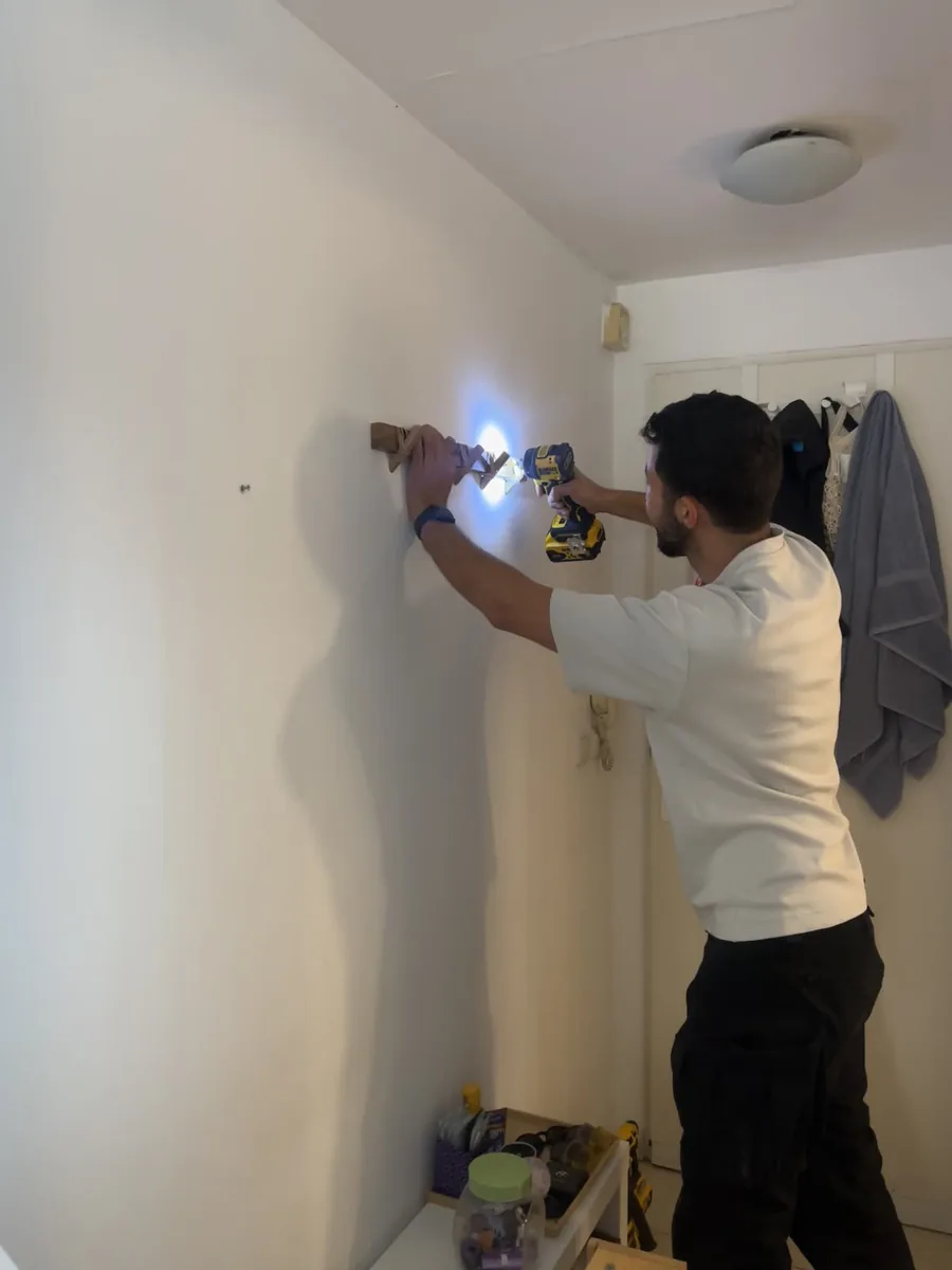רועי מבריג בורג לקיר בעזרת מברגת אימפקט צהובה עם נורית תאורה